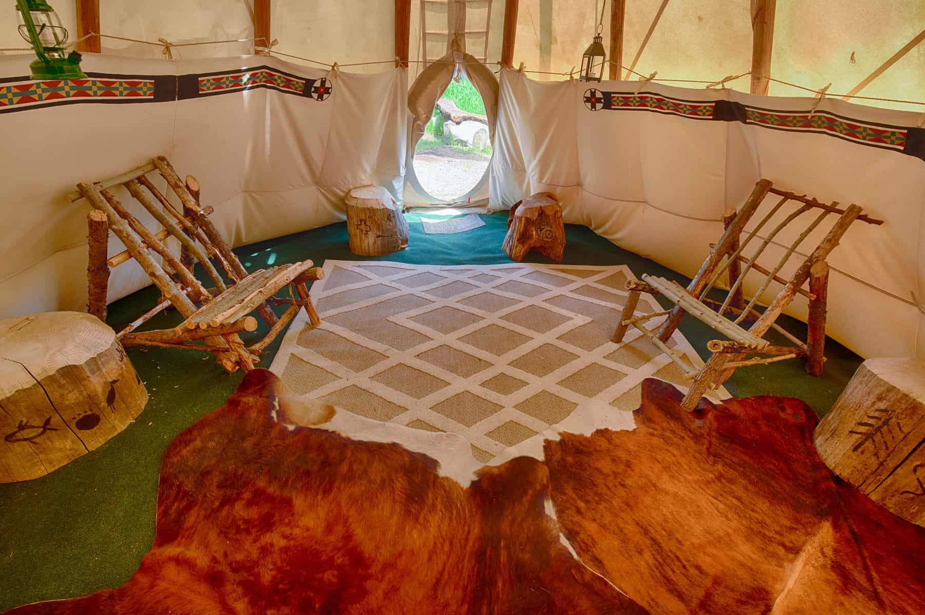 Teepee camping interior with carpet, rug, cowhides, log furniture and Indian artifacts.