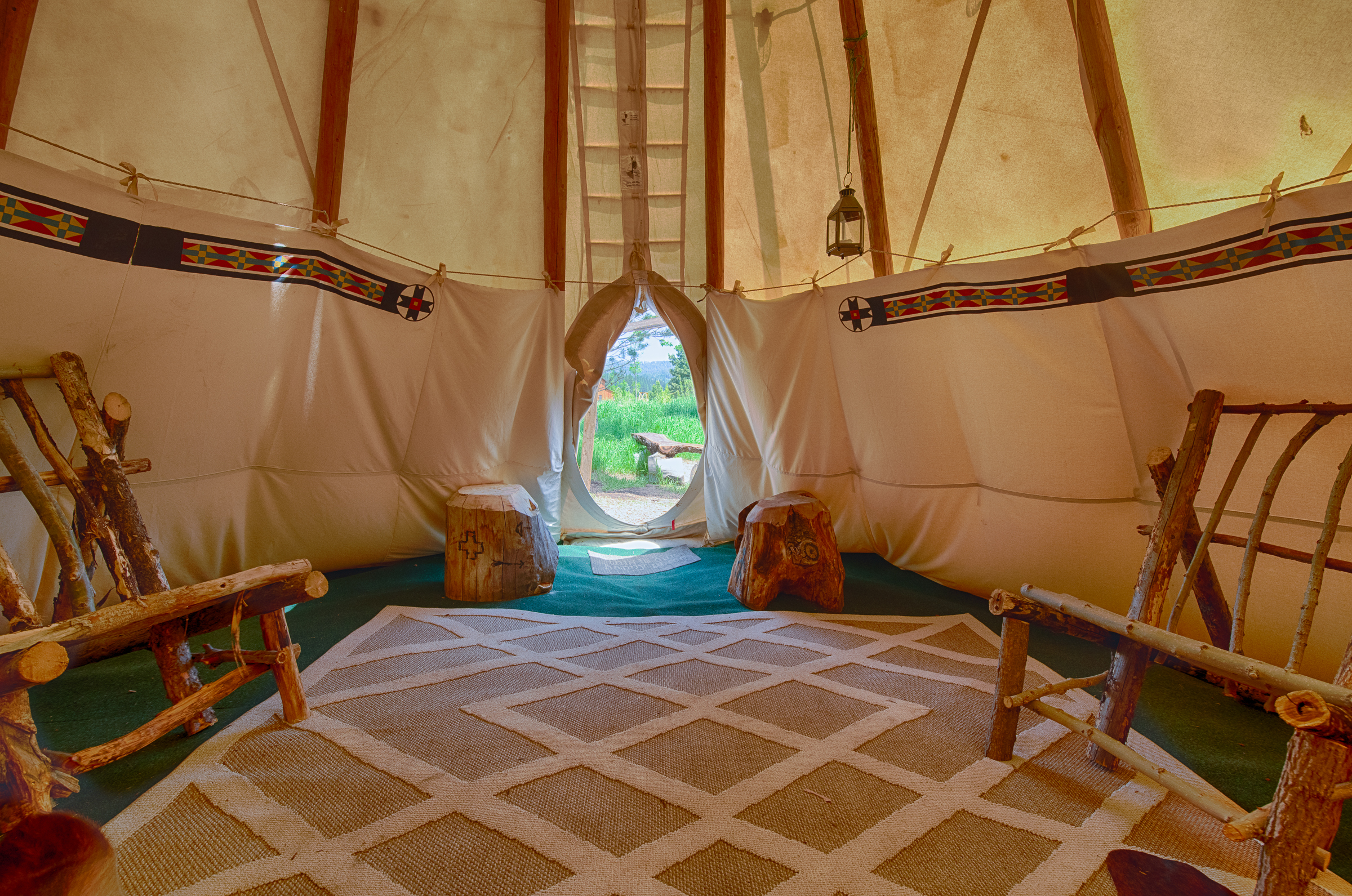 Tipi interior with custom log furniture, wall to wall carpeting and an area rug. Decorated with American Indian  content.